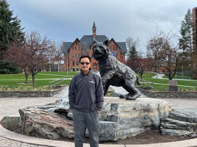 Weinan Leng poses with a bronze sculpture of Montana State's first bobcat, the centerpiece of Alumni Plaza on MSU's campus, MONT