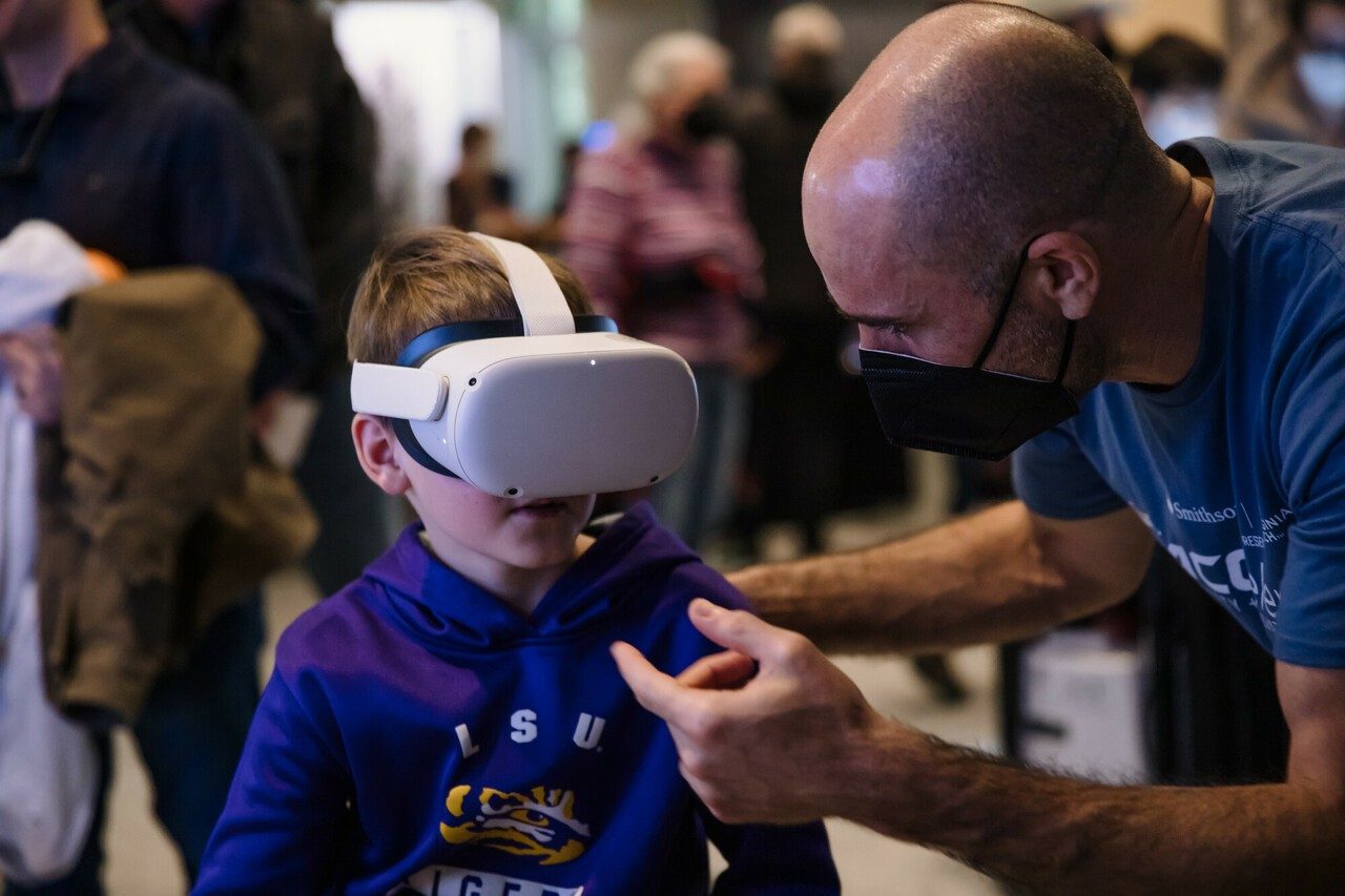 Faculty member Justin Perkinson helps a child in a VR headset at the Benthos 360 exhibit