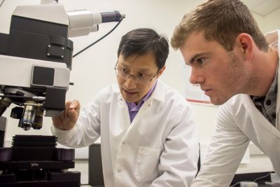 Weinan Leng explains microscope to a student